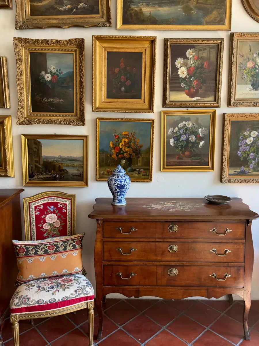 Antique walnut commode and tapestry chair beneath a wall of gilt-framed paintings