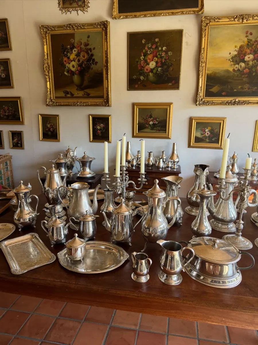 Table crowded with antique sterling silver teapots, candlesticks and trays
